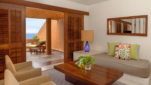 A room with a wooden sofa, a coffee table with a plant, a mirror, and a view of the sea through a wooden door.