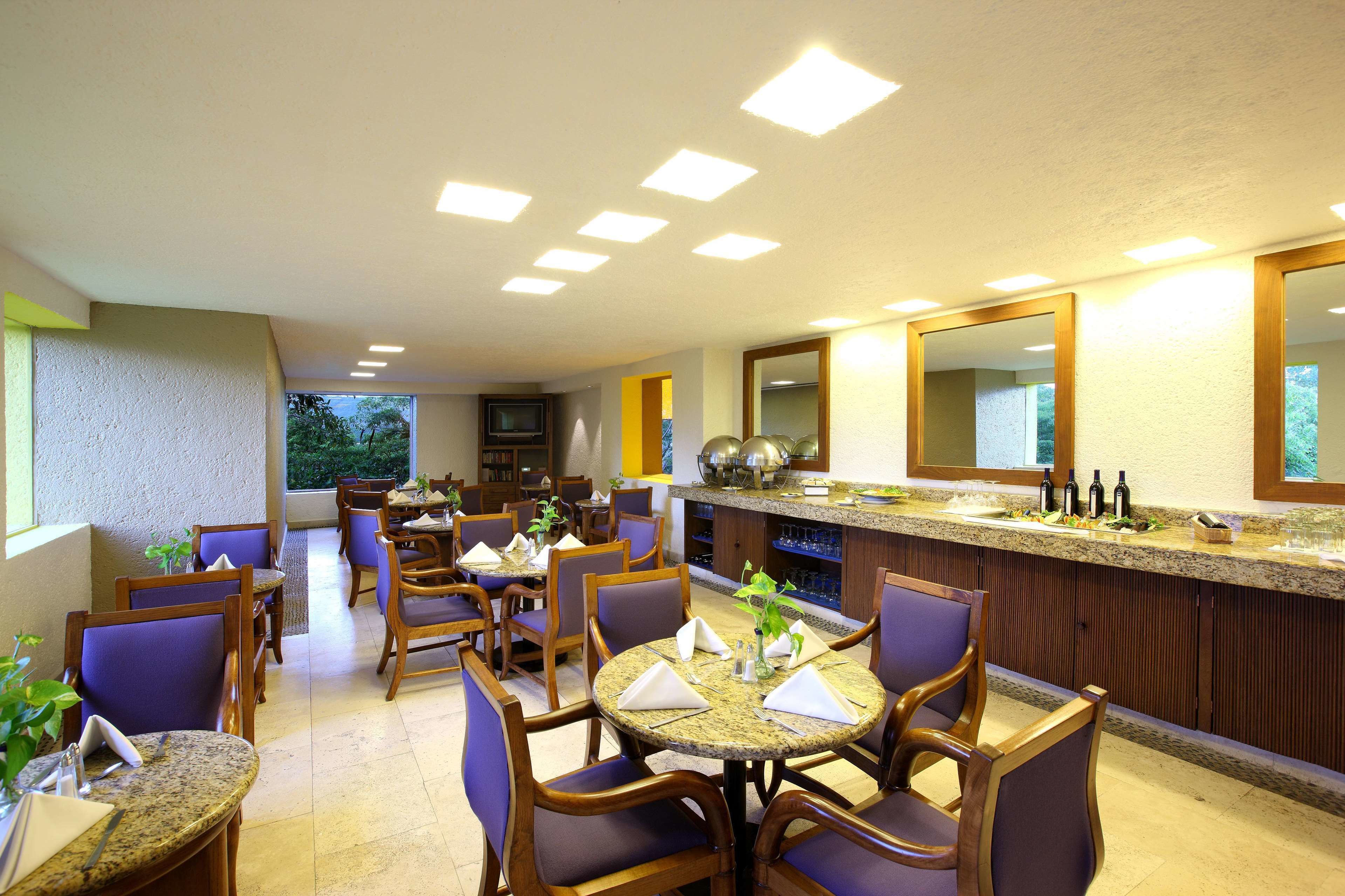 A restaurant with round tables, purple chairs, and a bar area with a mirror and bottles.