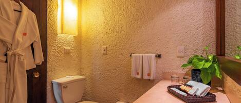 A bathroom with a toilet, sink, and a mirror. There is a towel rack with towels and a plant on the counter.