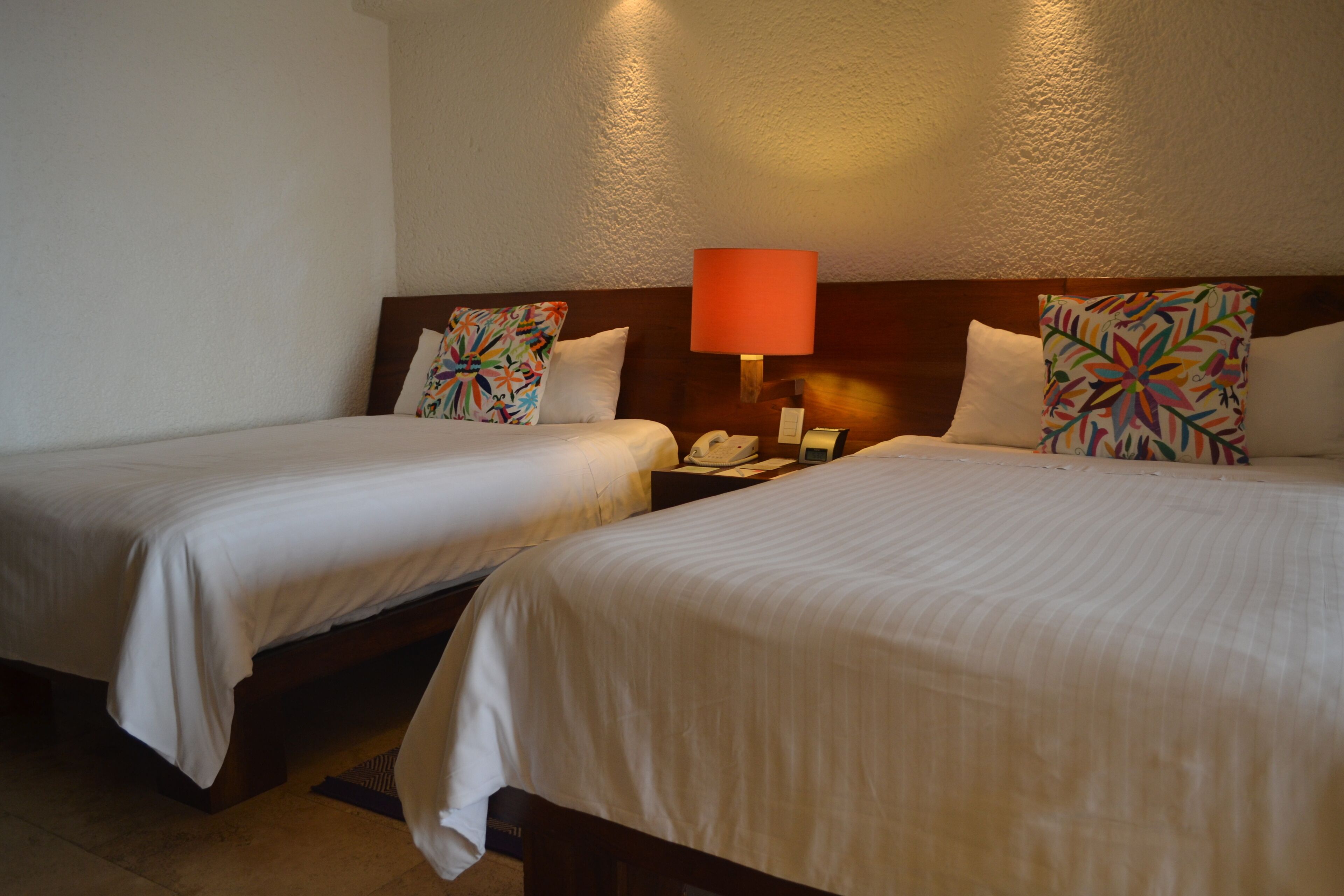 Two single beds with white linens, a wooden headboard, a bedside table with a lamp, and a telephone.