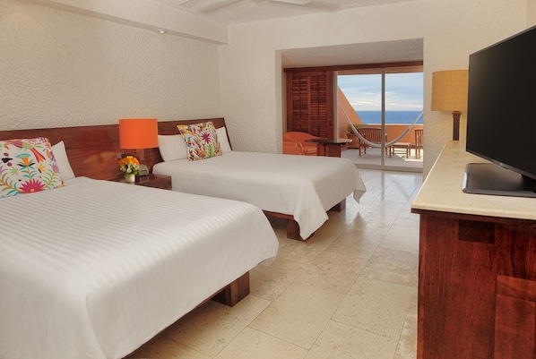 A hotel room with two beds, a TV, a balcony with a view, and a table with a lamp. - Las Brisas Ixtapa (Ixtapa)