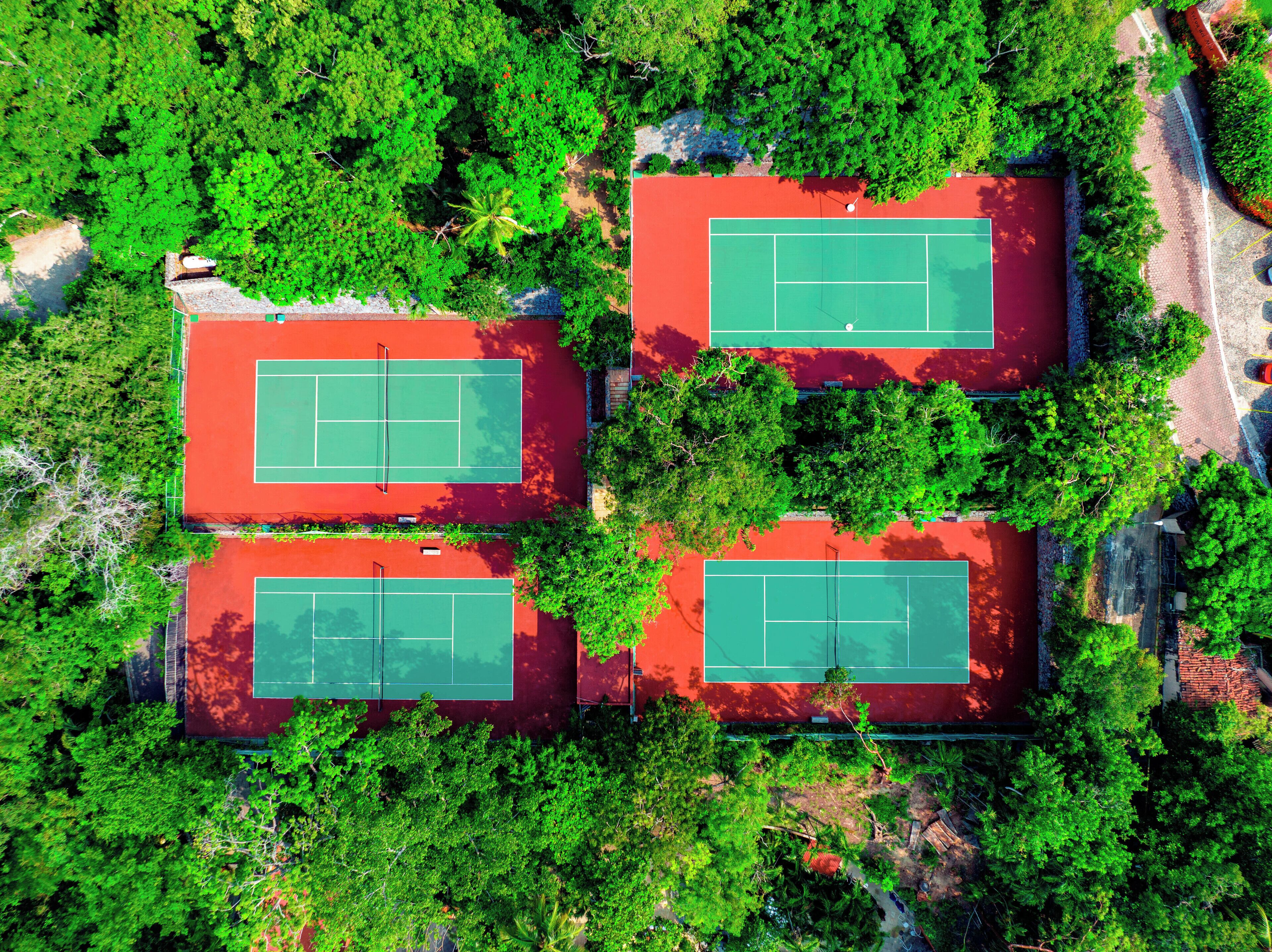 An aerial view of a tennis court complex surrounded by dense greenery.