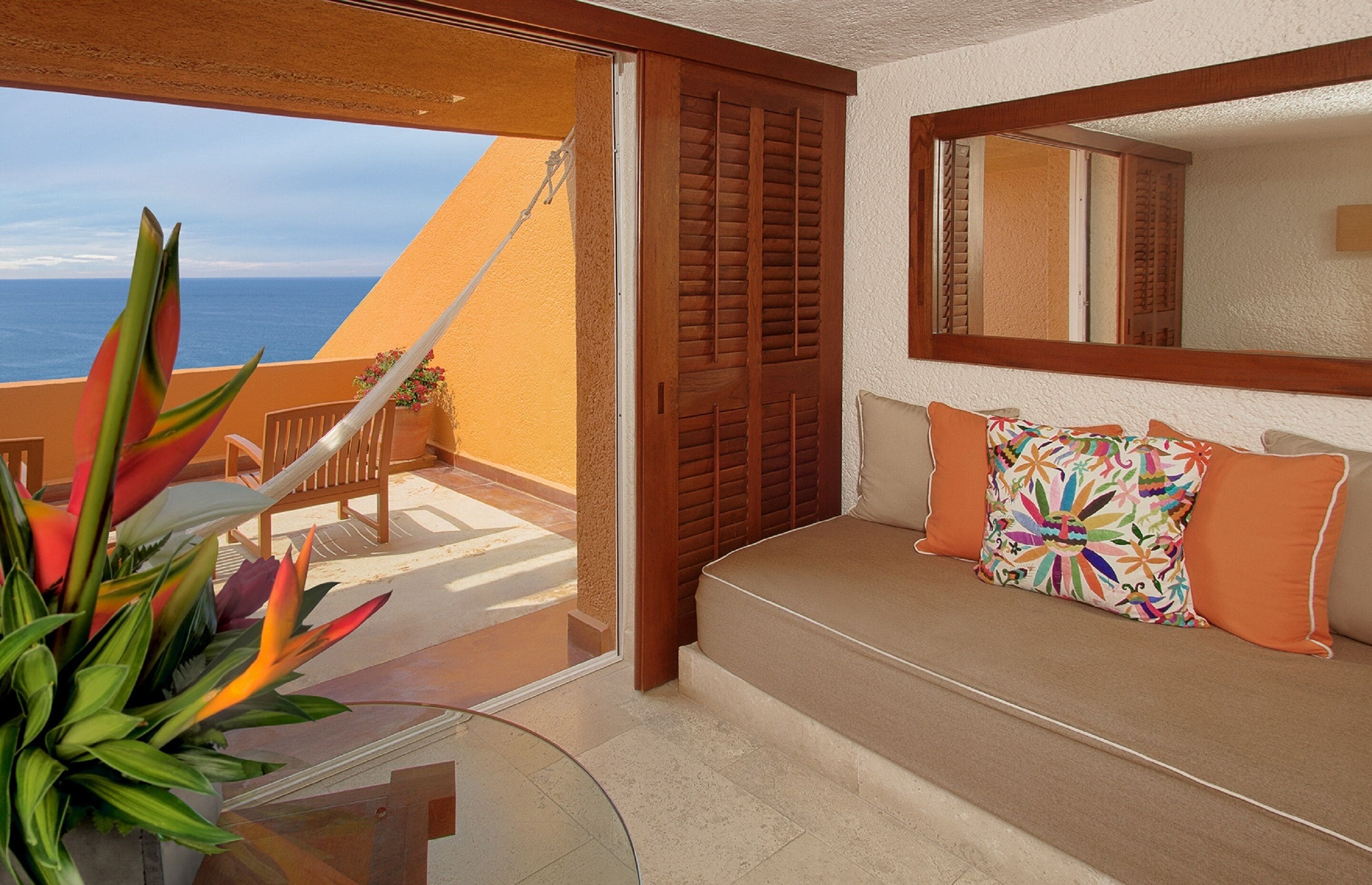 Un balcon avec vue sur la mer, un canapé agrémenté de coussins colorés et un grand miroir.
