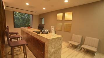 A modern kitchen with a marble countertop, bar stools, a built-in oven, and a window with a view of greenery.