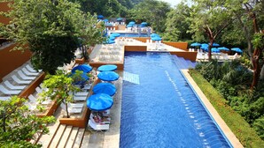 A swimming pool with lounge chairs and umbrellas, surrounded by greenery.
