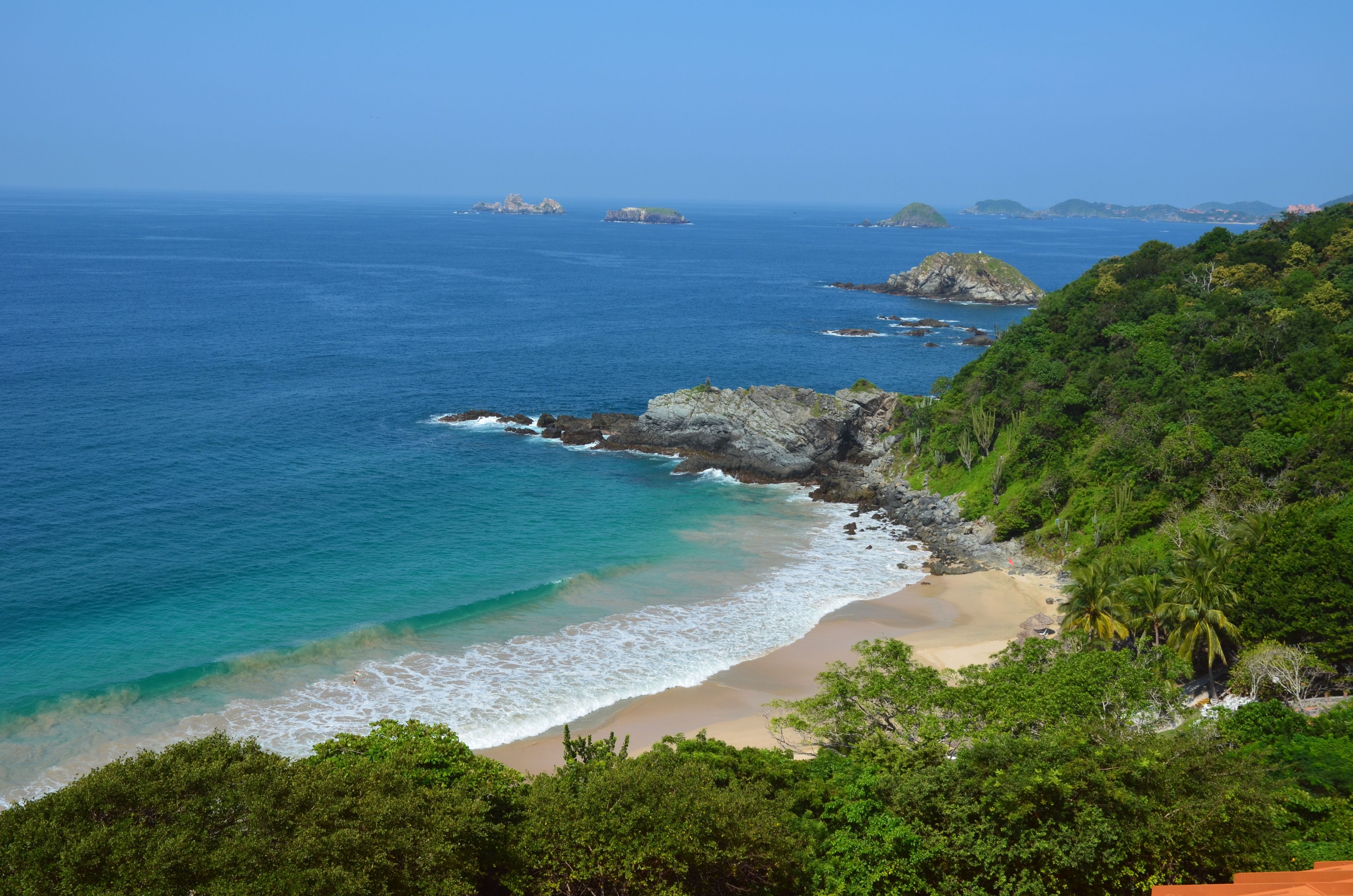 A coastal landscape with a beach, rocky outcrops, and dense greenery.