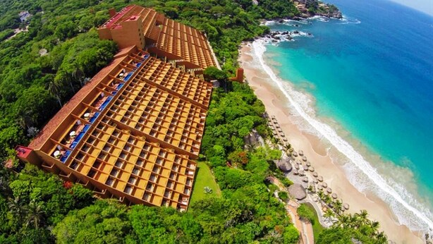 An aerial view of a resort with multiple bungalow-style buildings, a beach, and a rocky coastline.