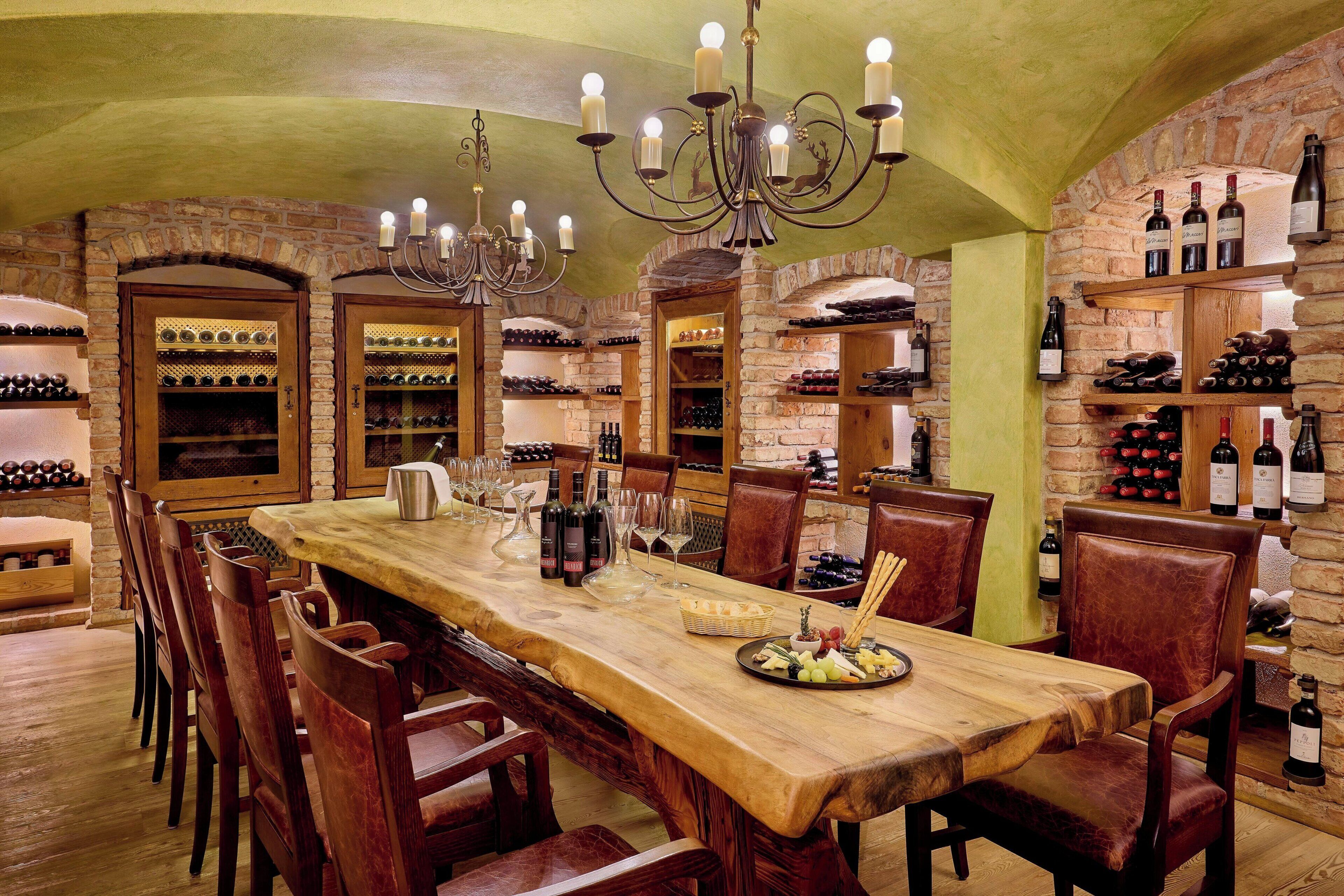 A long wooden dining table with chairs, surrounded by wine racks and shelves with bottles.