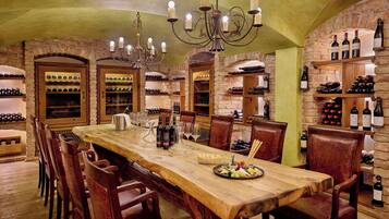A long wooden dining table with chairs, surrounded by wine racks and shelves with bottles.