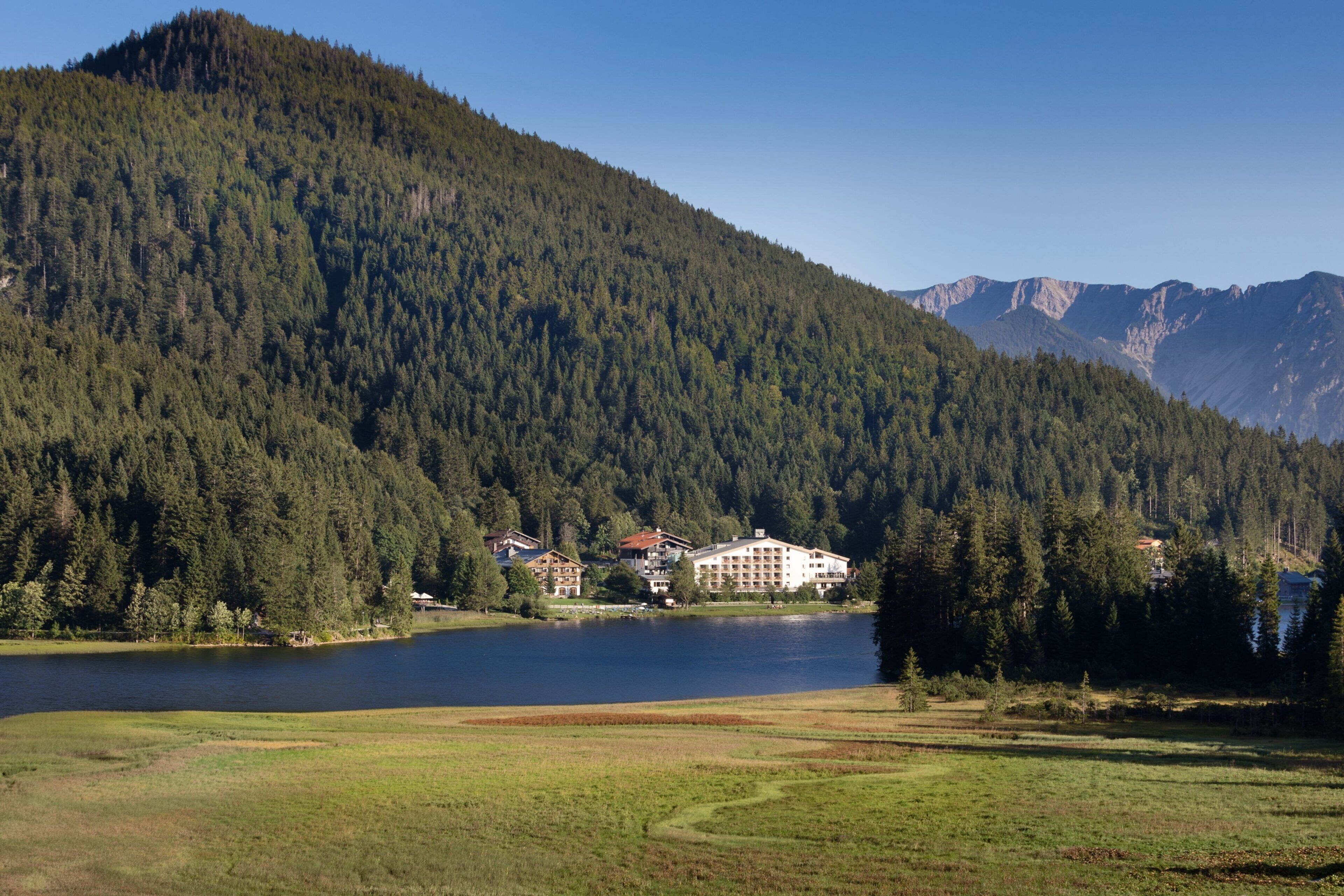 Eine Berglandschaft mit einem See, einem mehrstöckigen Hotel und einem bewaldeten Gebiet.