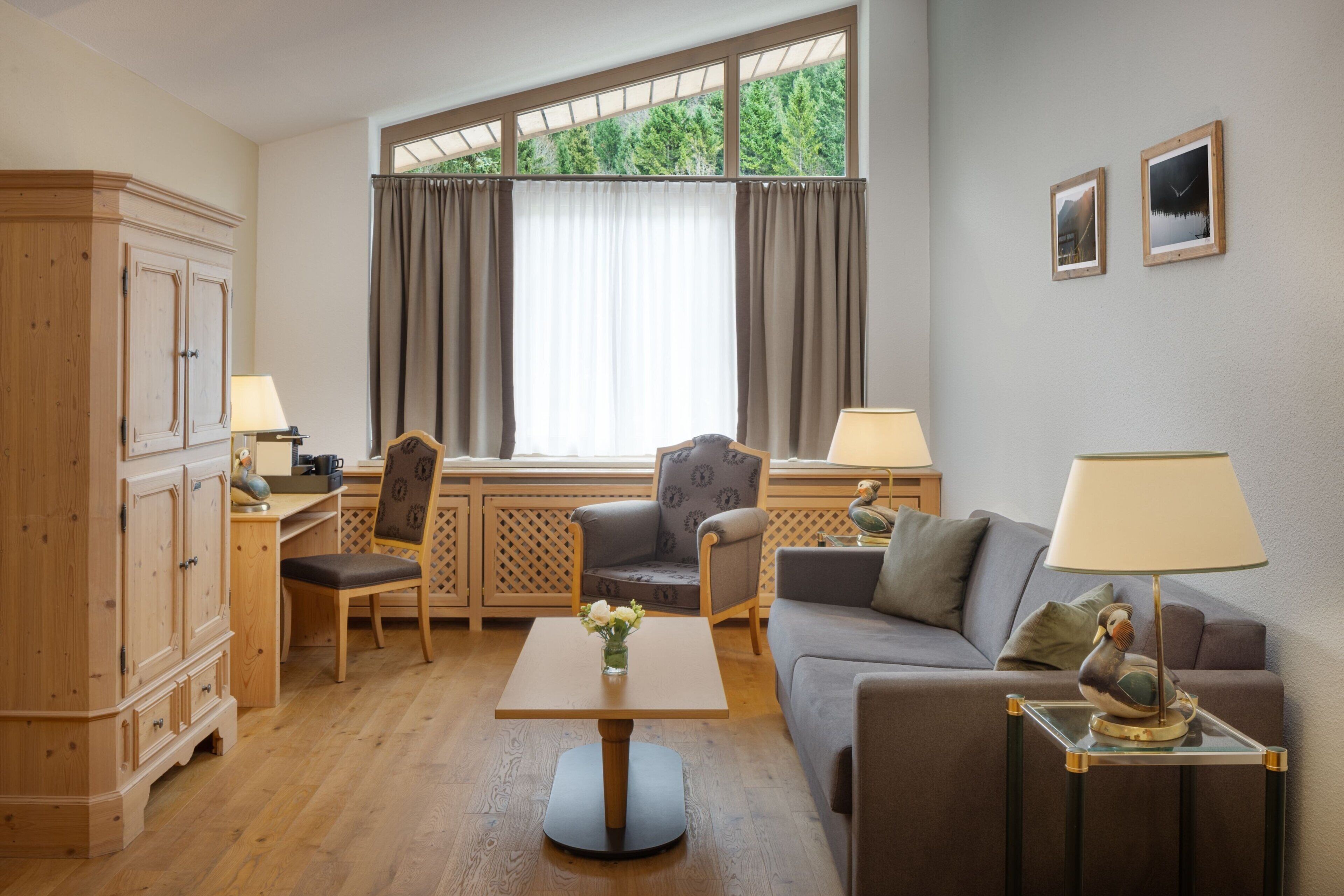 A well-lit room with a wooden cabinet, a desk with a chair, a sofa, and a table with a lamp.