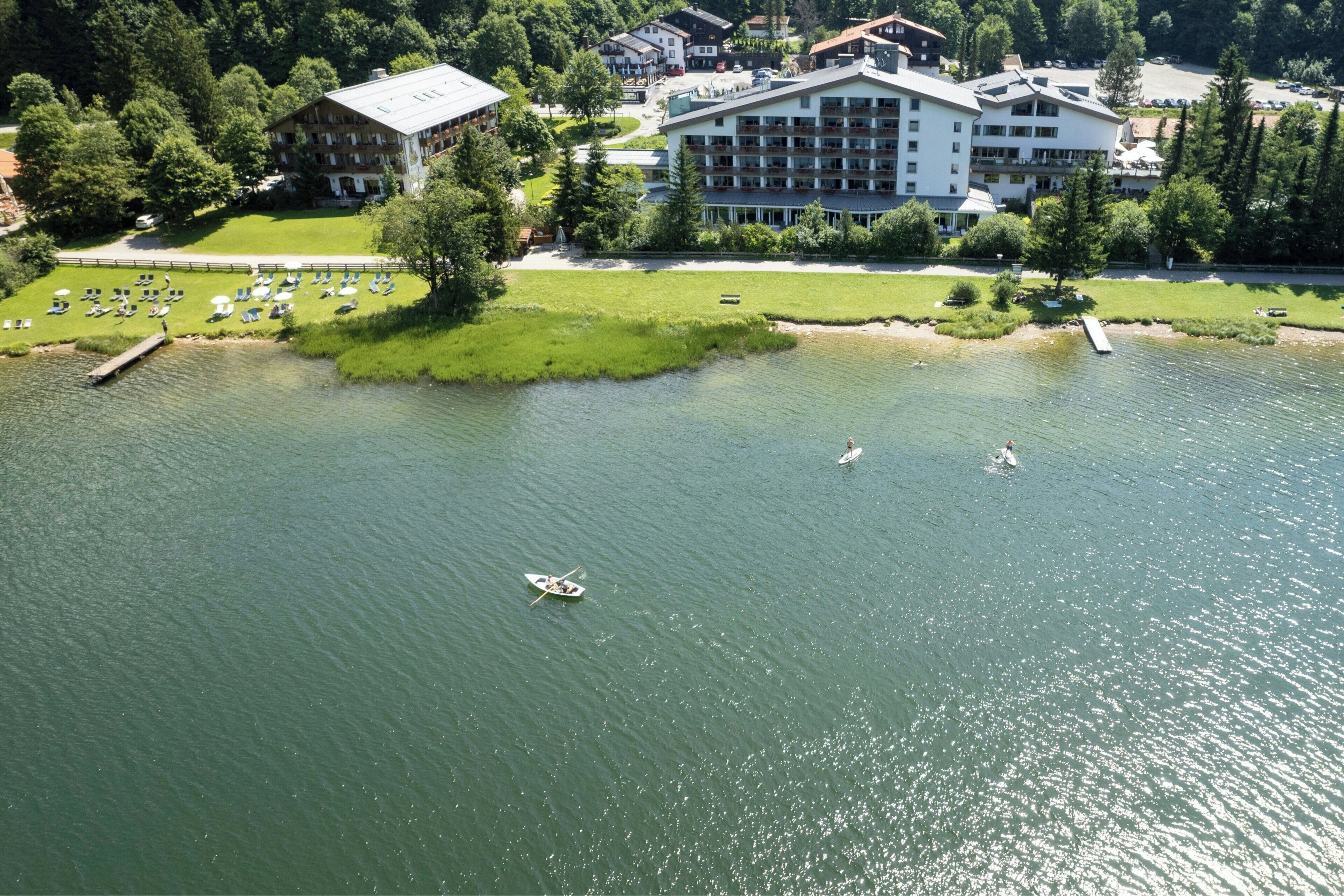 An aerial view of a lakeside hotel with a swimming area, a dock, and a well-maintained lawn.