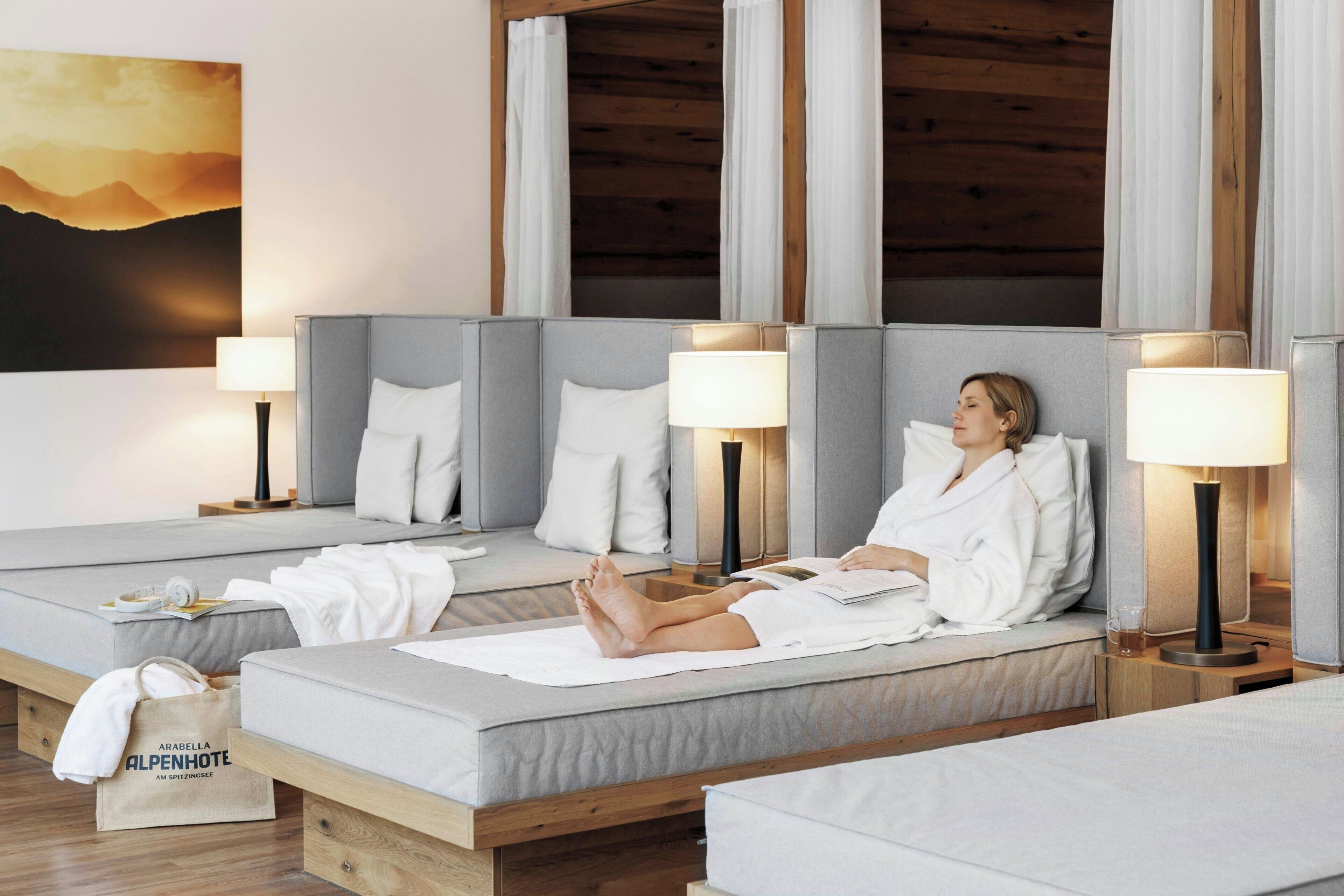 A spa suite with two beds, each with a bedside table and lamp, a wooden ceiling, and a painting of mountains.