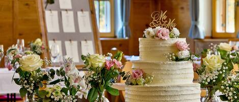 Un pastel de bodas de varios niveles decorado con flores y un adorno en la parte superior, rodeado de pequeños jarrones de flores sobre una mesa de madera.