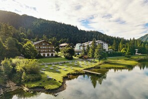 A lakeside hotel with multiple buildings, a grassy area with sun loungers, and a forested mountain backdrop. - Arabella Alpenhotel am Spitzingsee, a Tribute Portfolio Hotel (Schliersee)