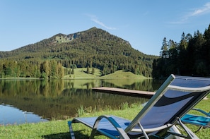 Vista del lago con una montaña al fondo, un muelle de madera y una silla de descanso junto al agua.
