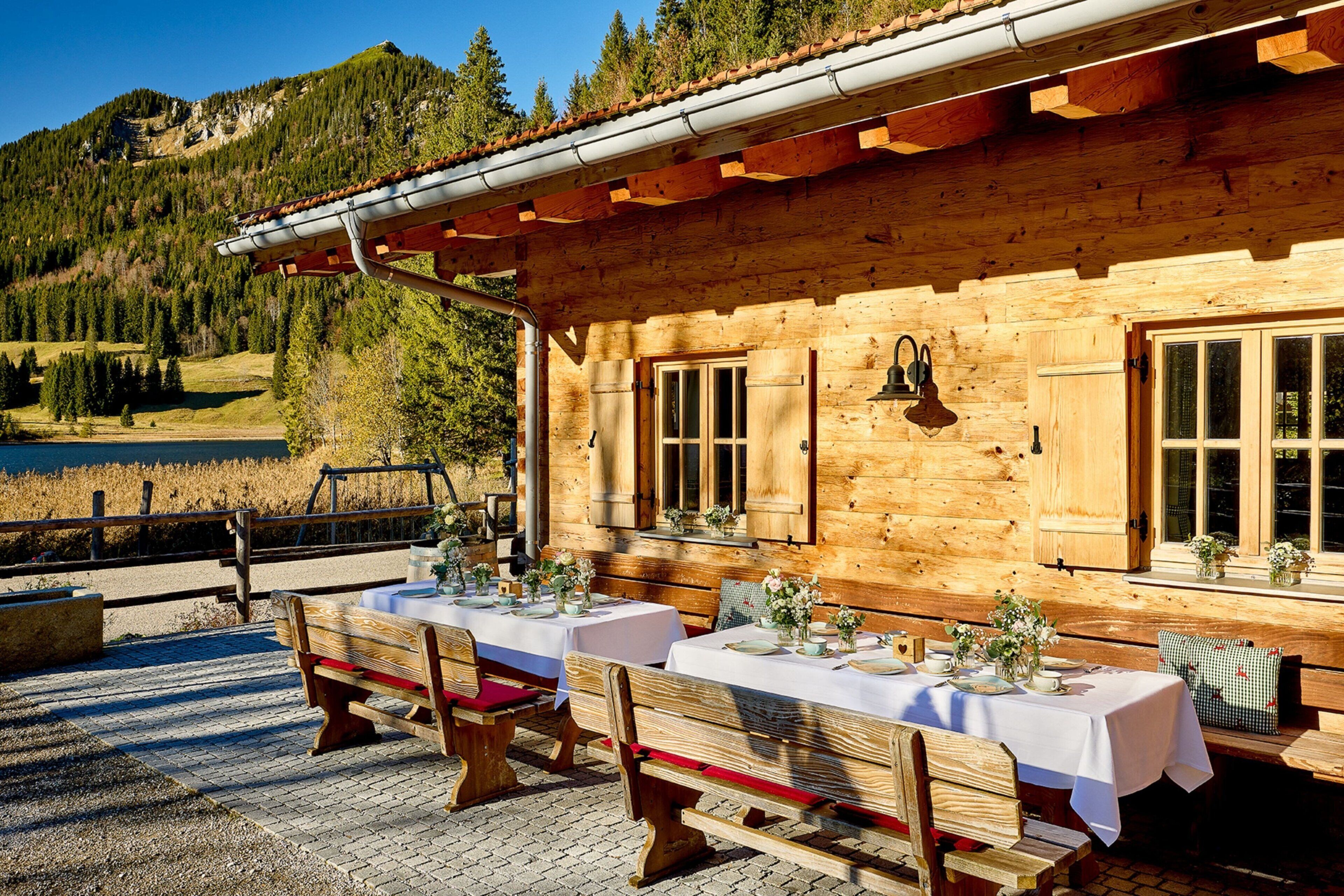 A wooden cabin with a dining area set up outside, featuring tables and benches.