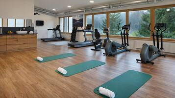 Une salle de sport équipée de tapis de course, de vélos elliptiques et de tapis de sol pour les exercices.
