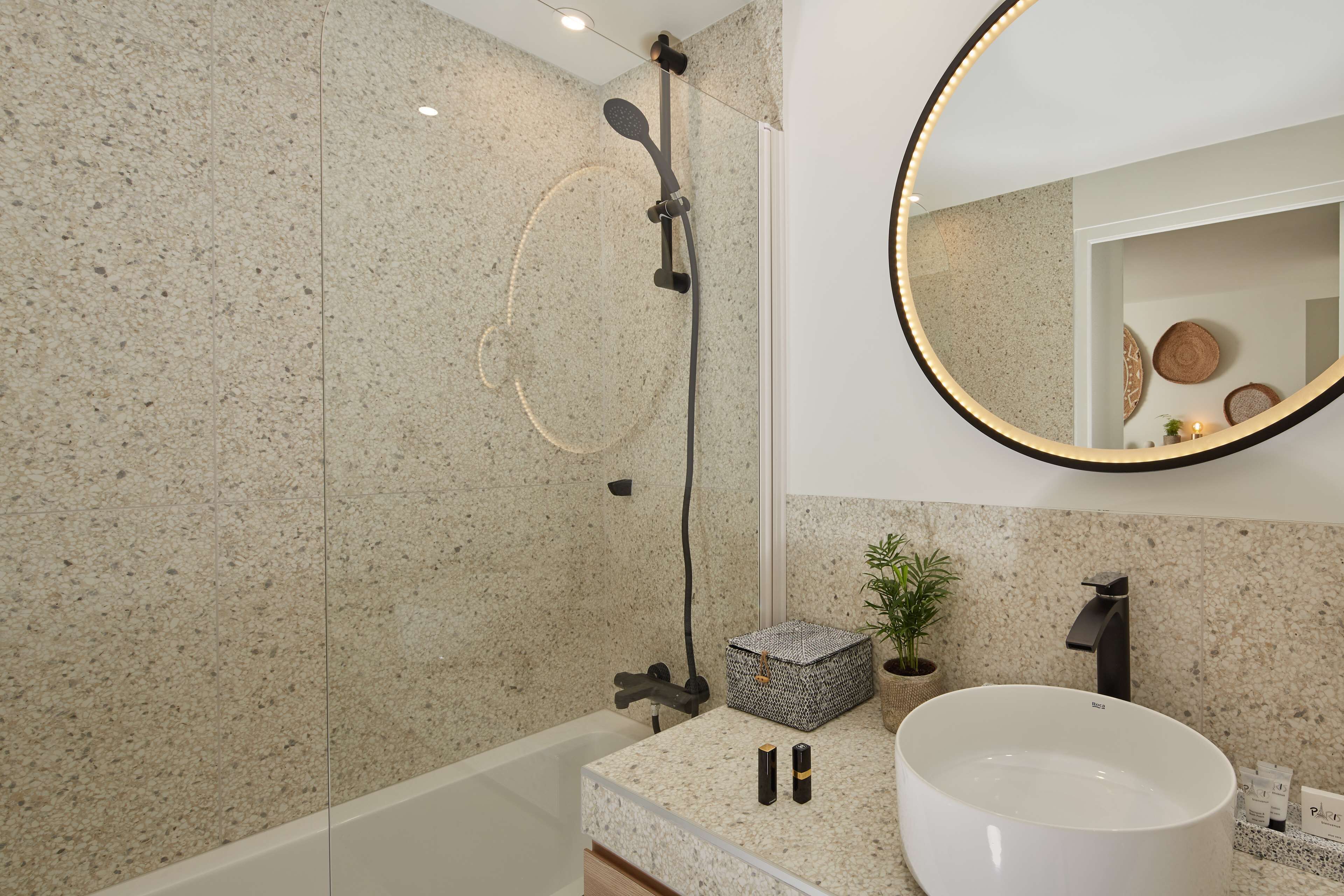 A modern bathroom with a freestanding bathtub, a large mirror, and a granite countertop.