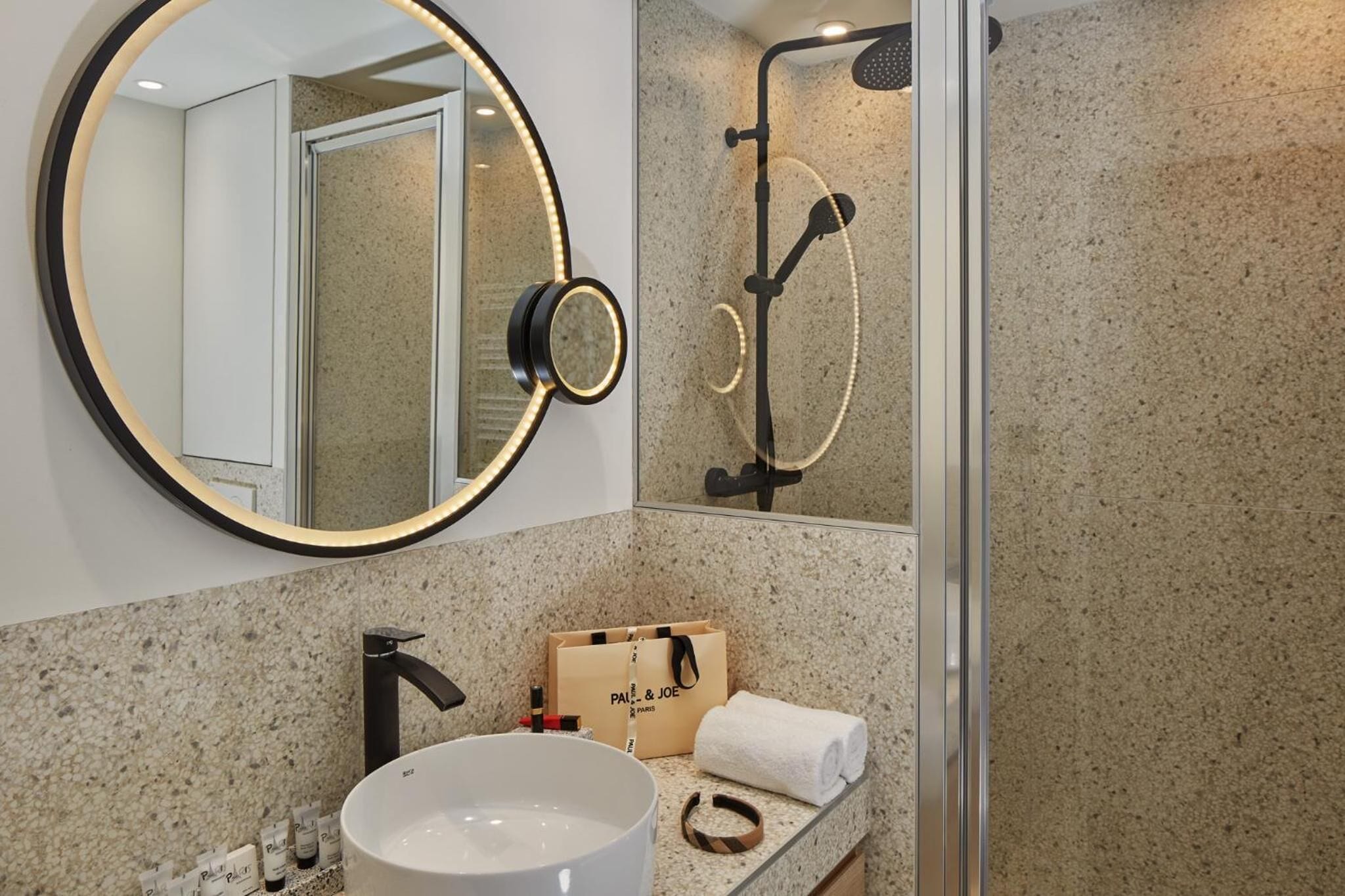 A bathroom with a round mirror, a shower, a sink, and a towel.