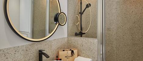 A bathroom with a round mirror, a shower, a sink, and a towel.