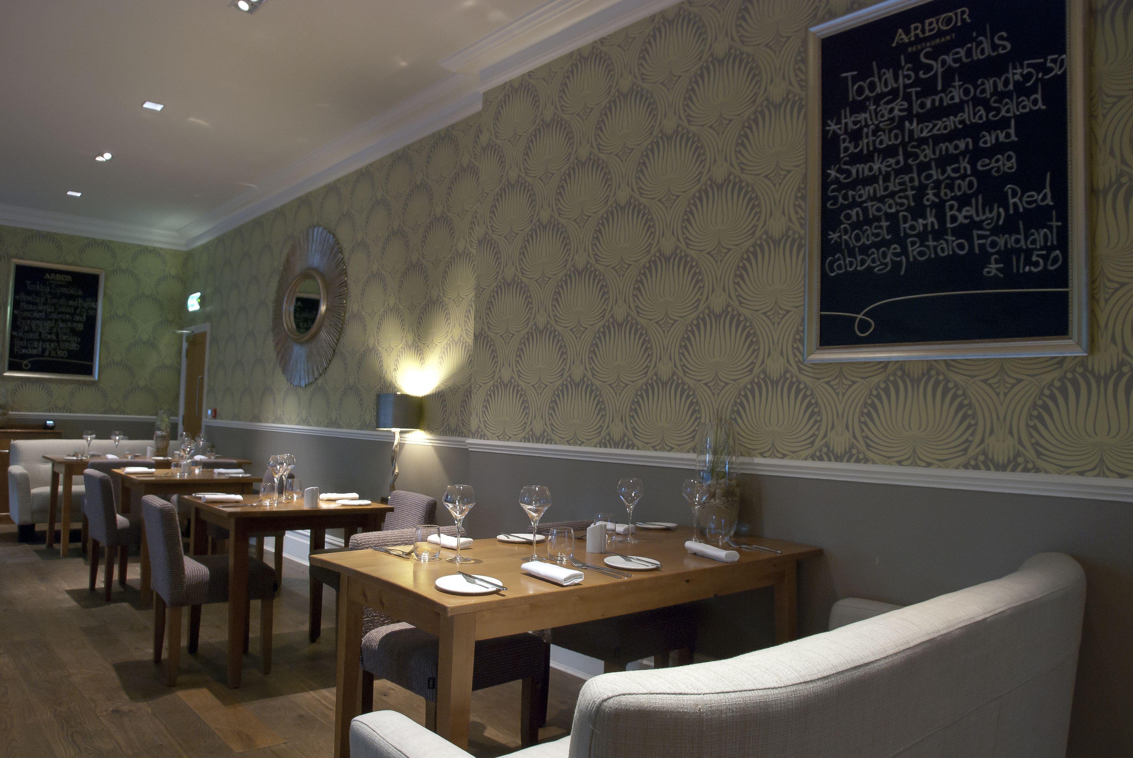 Een restaurant interieur met houten tafels en stoelen, een krijtbordmenu en behang met een patroon.