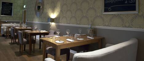 A restaurant interior with wooden tables and chairs, a chalkboard menu, and patterned wallpaper.