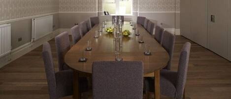 A conference room with a long table, eight chairs, and a window with blinds.