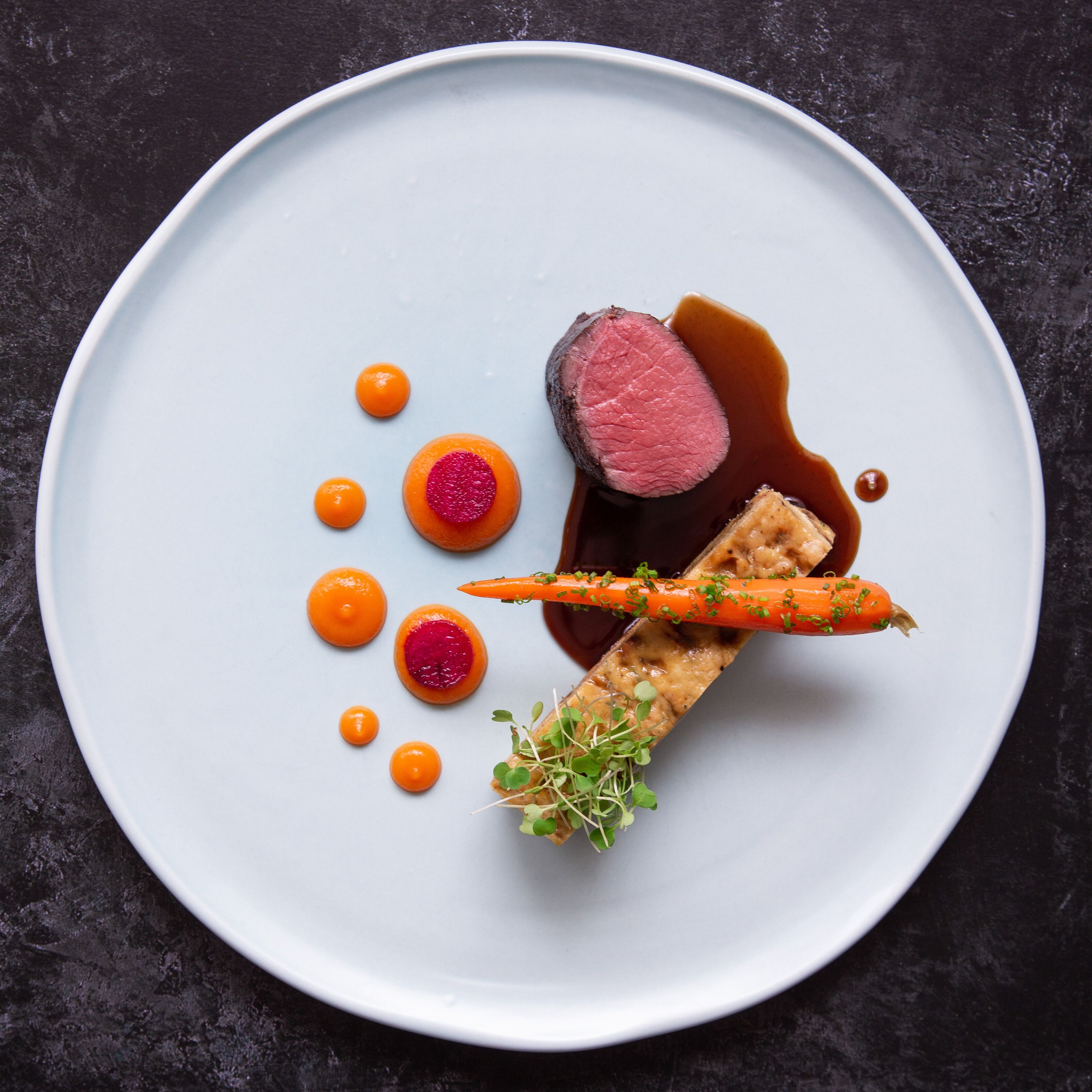 A plate with a steak, carrot, and sauce.