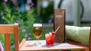 Una mesa de madera con una cerveza, un cóctel, un menú y un cojín verde.