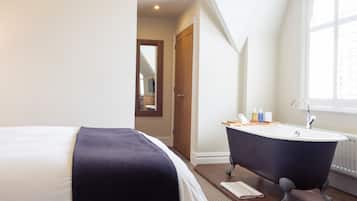 Une chambre avec un grand lit, une baignoire sur pieds et une fenêtre avec des stores.