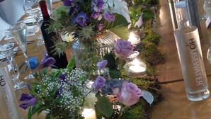 Une longue table ornée de compositions florales, de bouteilles de vin et de verres.