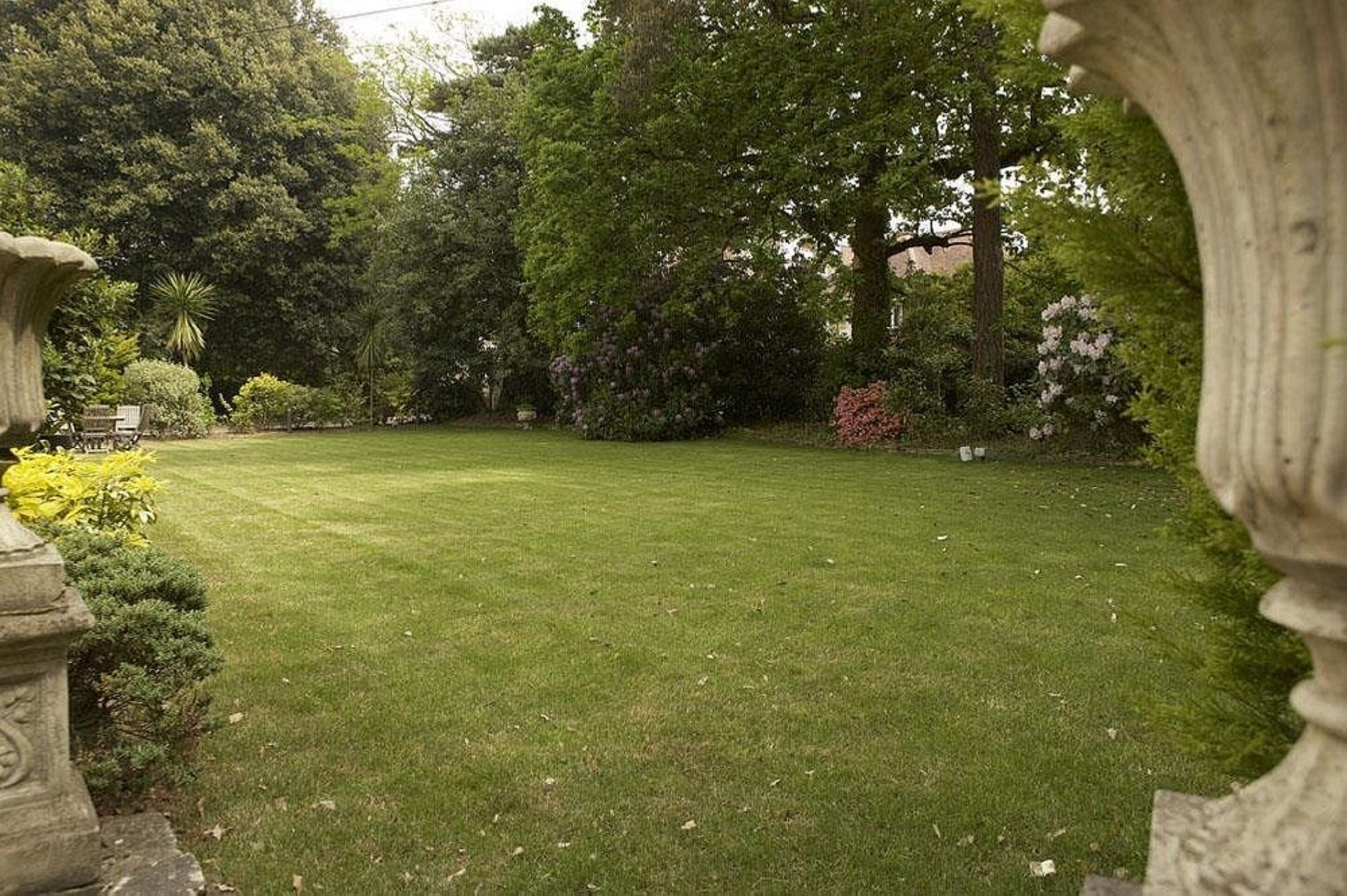 A well-maintained lawn with stone planters and a variety of shrubs and trees.