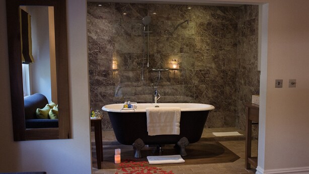 Une salle de bain avec une baignoire sur pieds, un miroir et une petite table sur laquelle est posée une bougie.