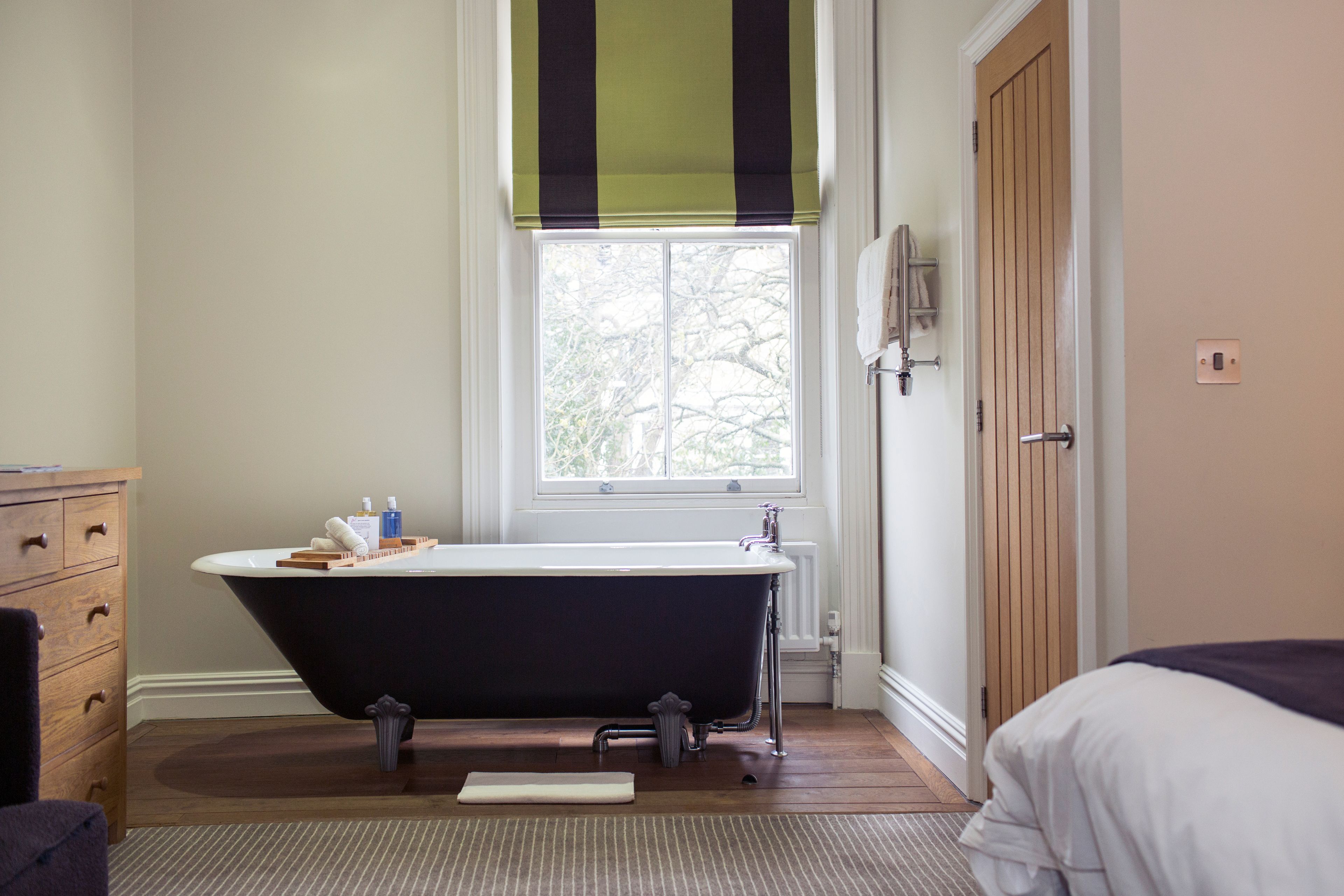 A bathroom with a freestanding bathtub, a wooden cabinet, a window with a view of trees, and a door with a towel rack.