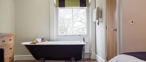 A bathroom with a freestanding bathtub, a wooden cabinet, a window with a view of trees, and a door with a towel rack.