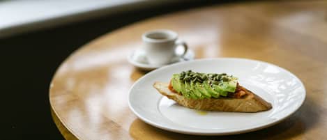 A round wooden table with a white plate containing a sandwich and a cup of coffee.