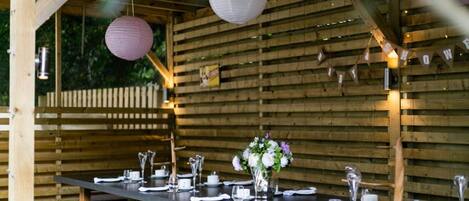 A wooden deck with a long table set for dining, surrounded by wooden walls and hanging paper lanterns.