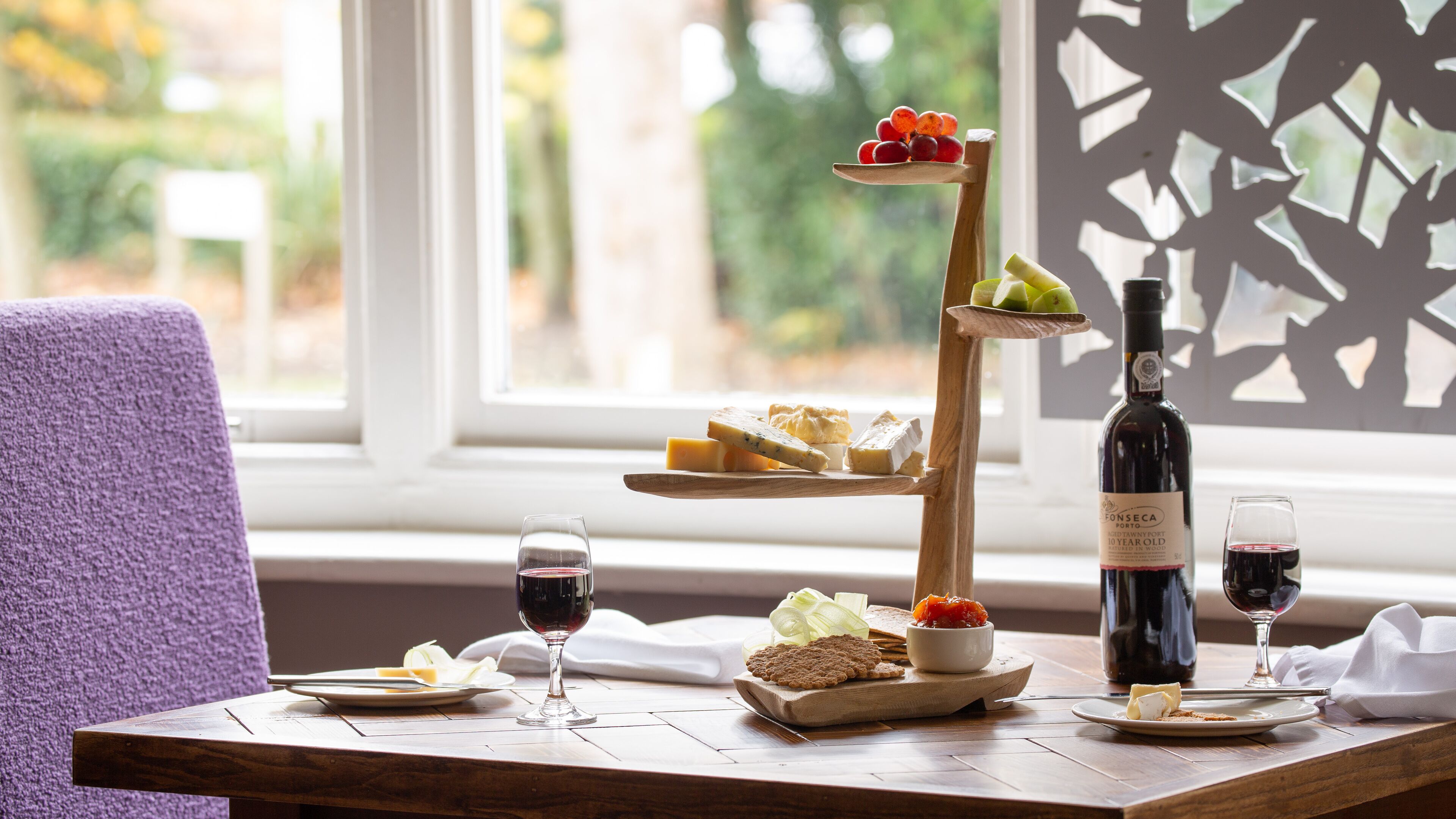 Una mesa de madera con una tabla de quesos, copas de vino y una botella.