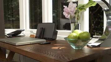 Un escritorio de madera con una computadora portátil, un teléfono, un control remoto, un cuenco de manzanas verdes y un florero con flores.