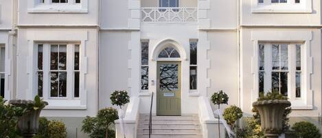 Un edificio imponente con una fachada simétrica, una entrada central con una puerta verde y una escalera que conduce a ella.