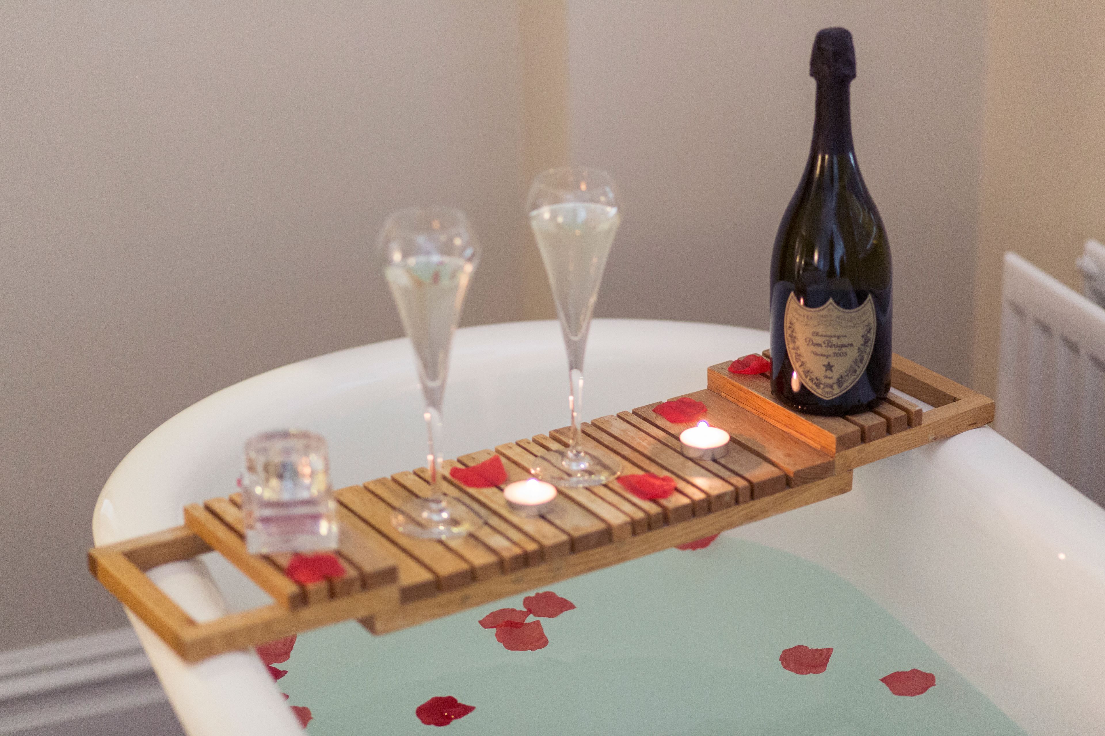 A bottle of champagne on a tray with glasses and candles on a bathroom counter.