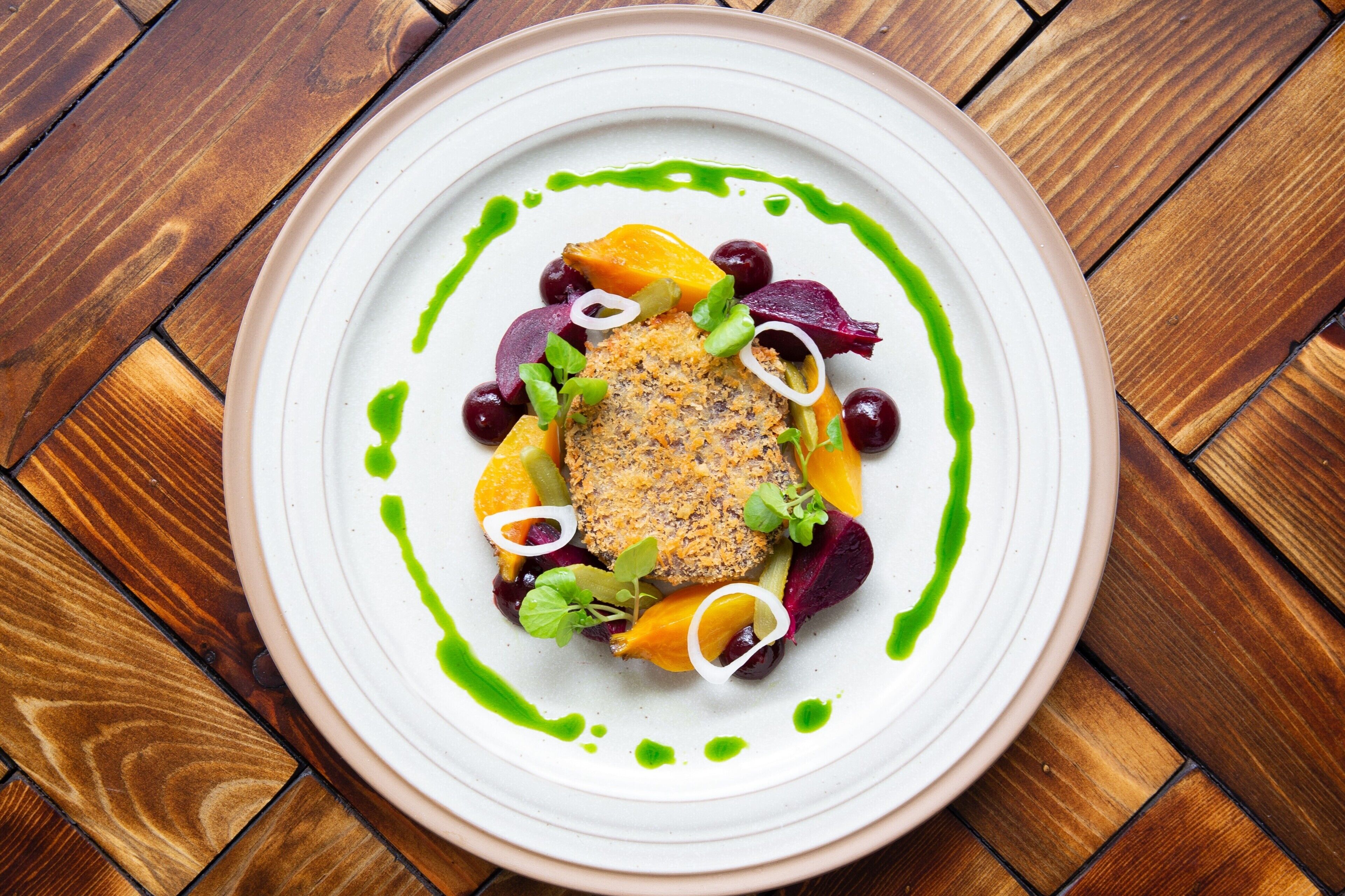 Une assiette de nourriture comprenant une variété de légumes et un morceau de viande, le tout garni d’une sauce verte et d’anneaux d’oignon blanc.