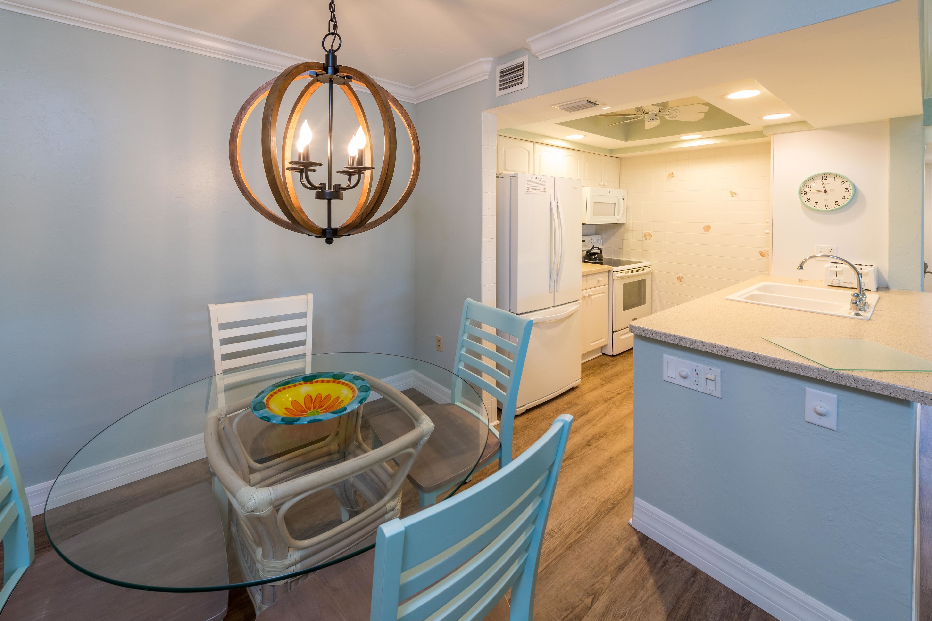 A dining area with a glass table, blue chairs, and a chandelier.