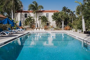 Relax by the serene pool surrounded by lush vegetation and palm trees, with lounge chairs and umbrellas at your disposal.
