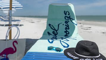 A beach chair with a towel and a hat, a striped umbrella, and a blue and white beach umbrella.