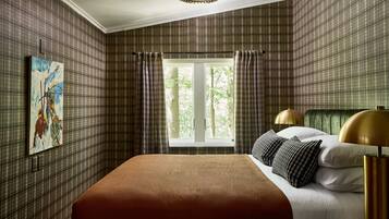 A bedroom with plaid wallpaper, a large bed with white and brown bedding, a painting on the wall, and a window with curtains.