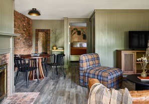 A cozy living room with a fireplace, a dining area with a round table and chairs, a plaid sofa, and a television.