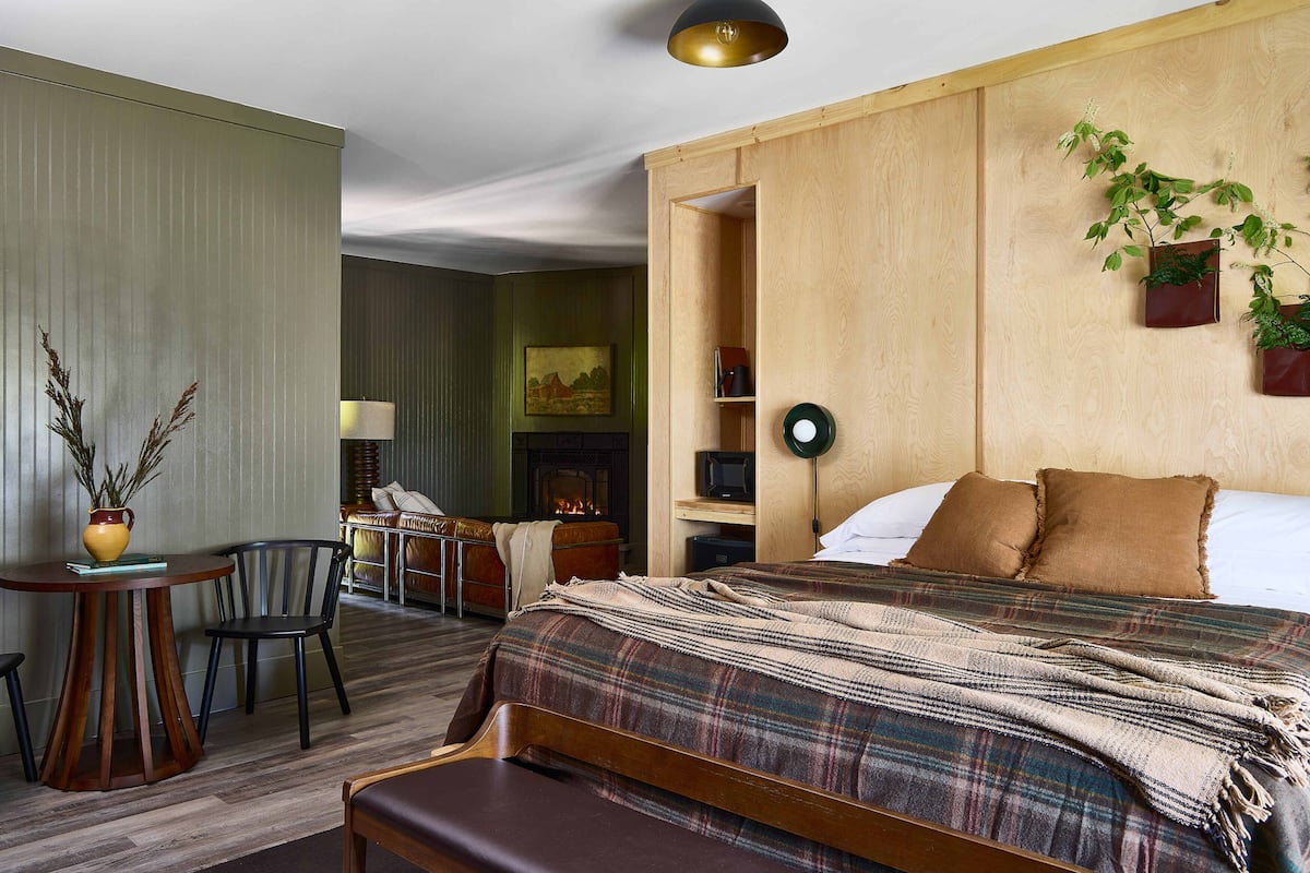 Hotellihuone, jossa on sänky, työpöytä, tuoli, takka ja ruukussa oleva kasvi.
