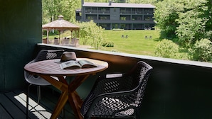 A balcony with a table and chairs, overlooking a lawn with a building and trees in the background. - Bluebird Cady Hill Lodge (Stowe)